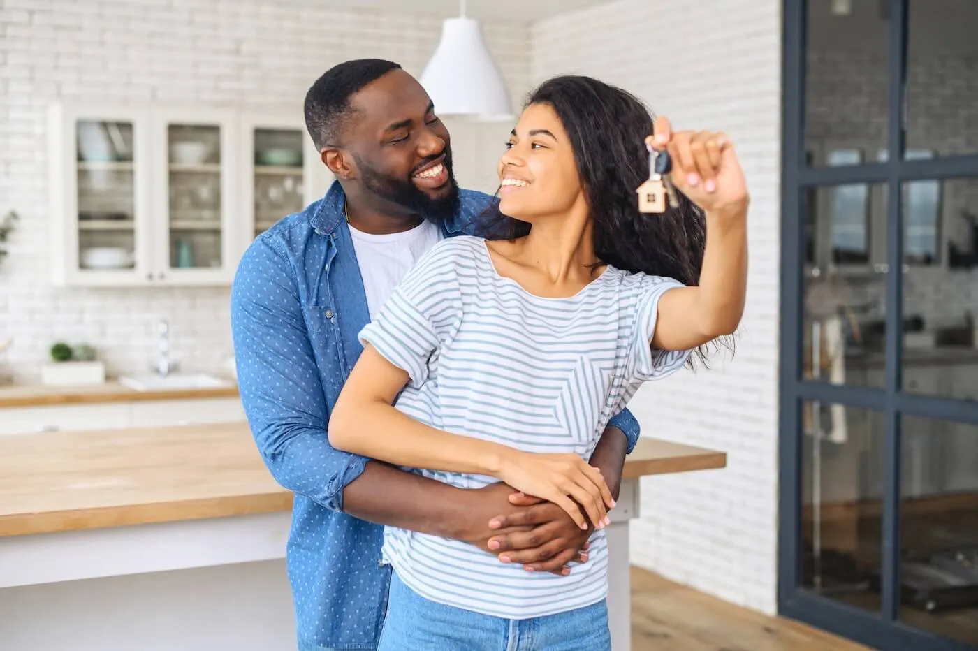 Happy couple embracing each other in the kitchen while the woman holds a house key on a keychain