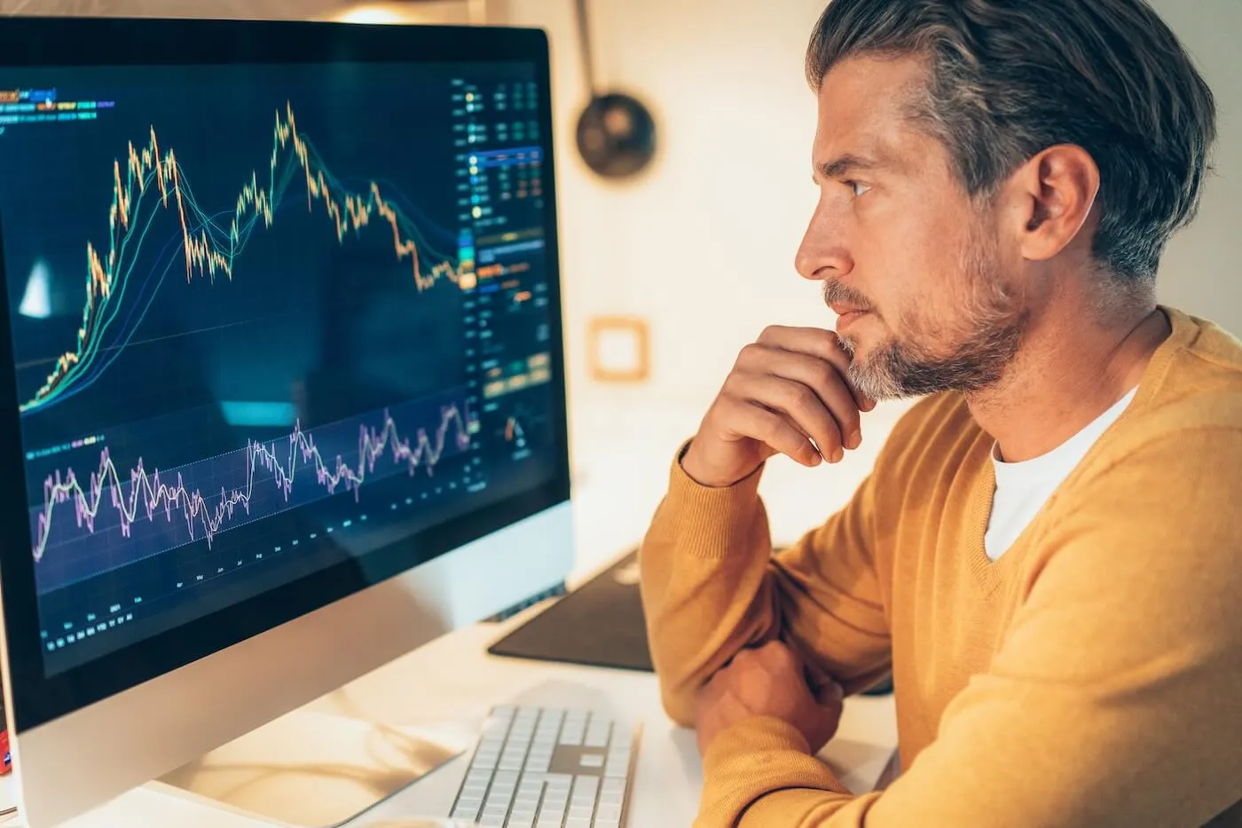 Pensive mature man looking at a large computer monitor displaying financial charts and graphs.