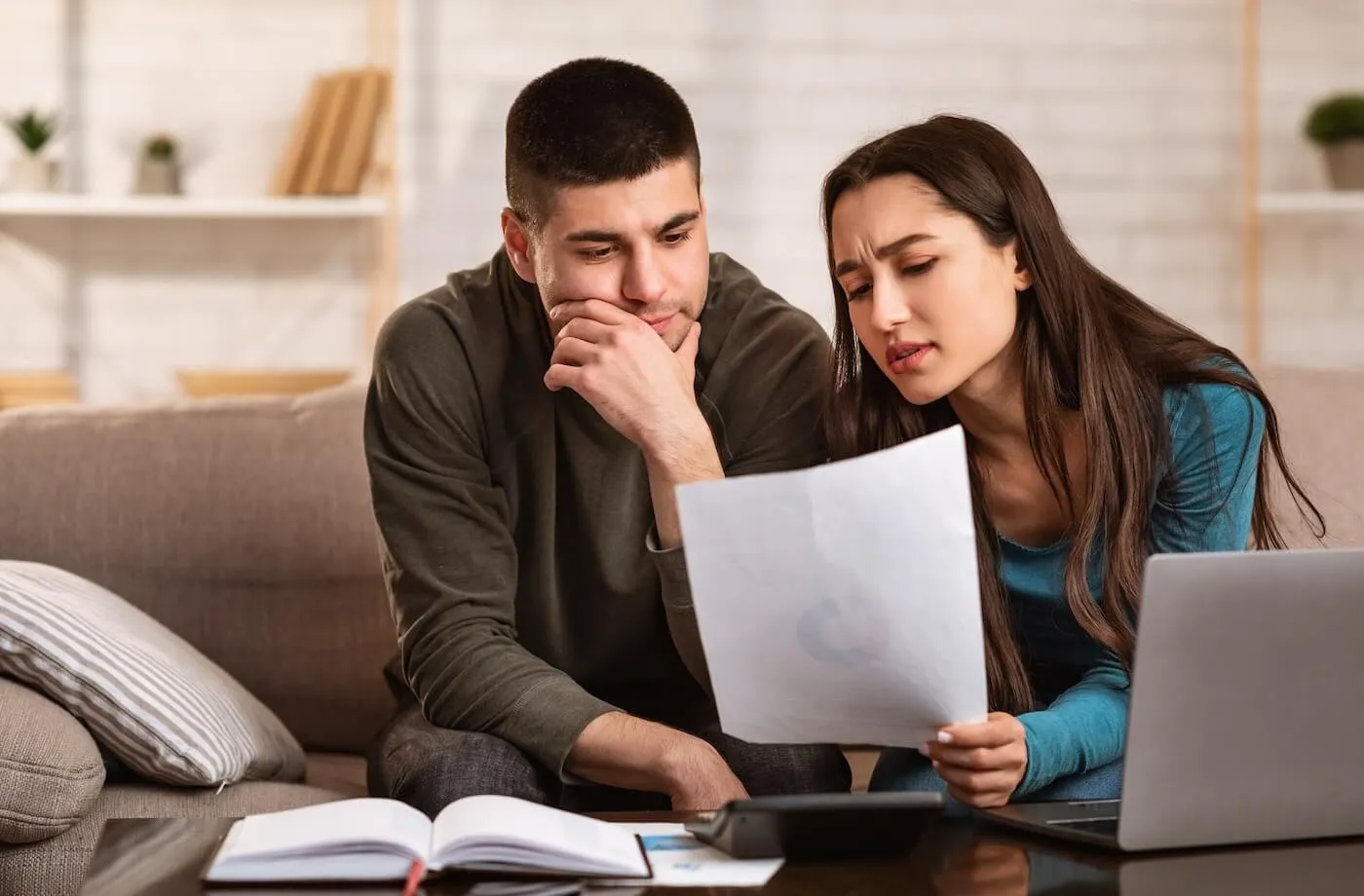 Concerned couple reviewing printed documents while sitting on the sofa in the living room
