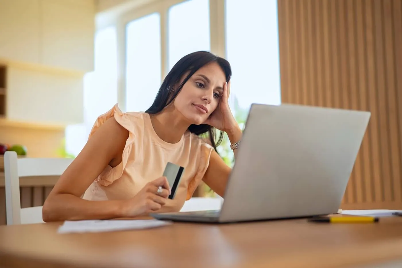 Pensive woman using her credit card online while sitting at the desk in the living room