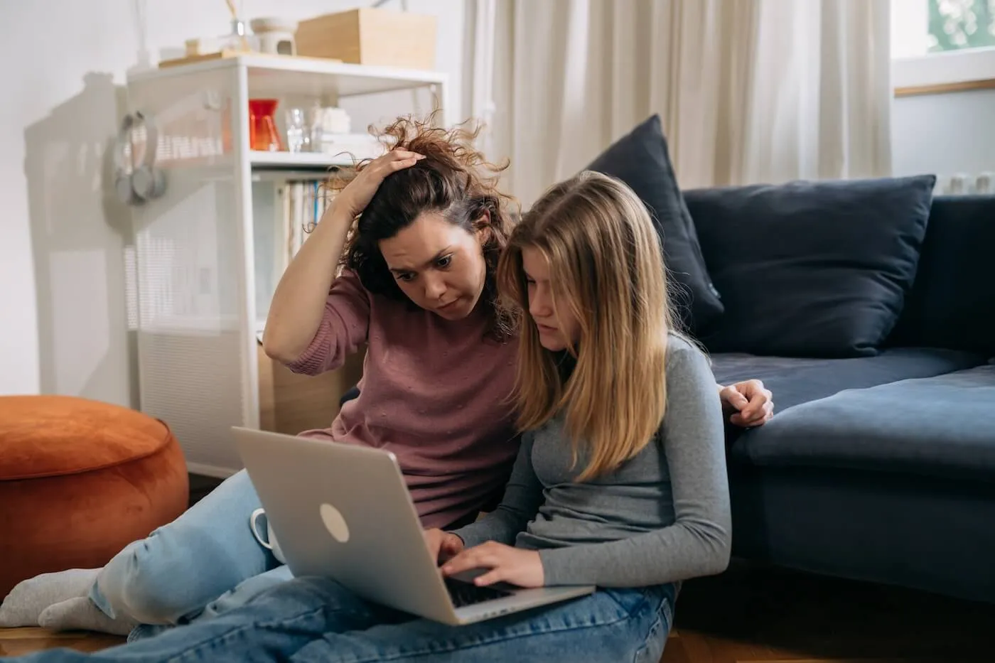 A mother and a teenage daughter sitting on the floor in the living room and using a laptop
