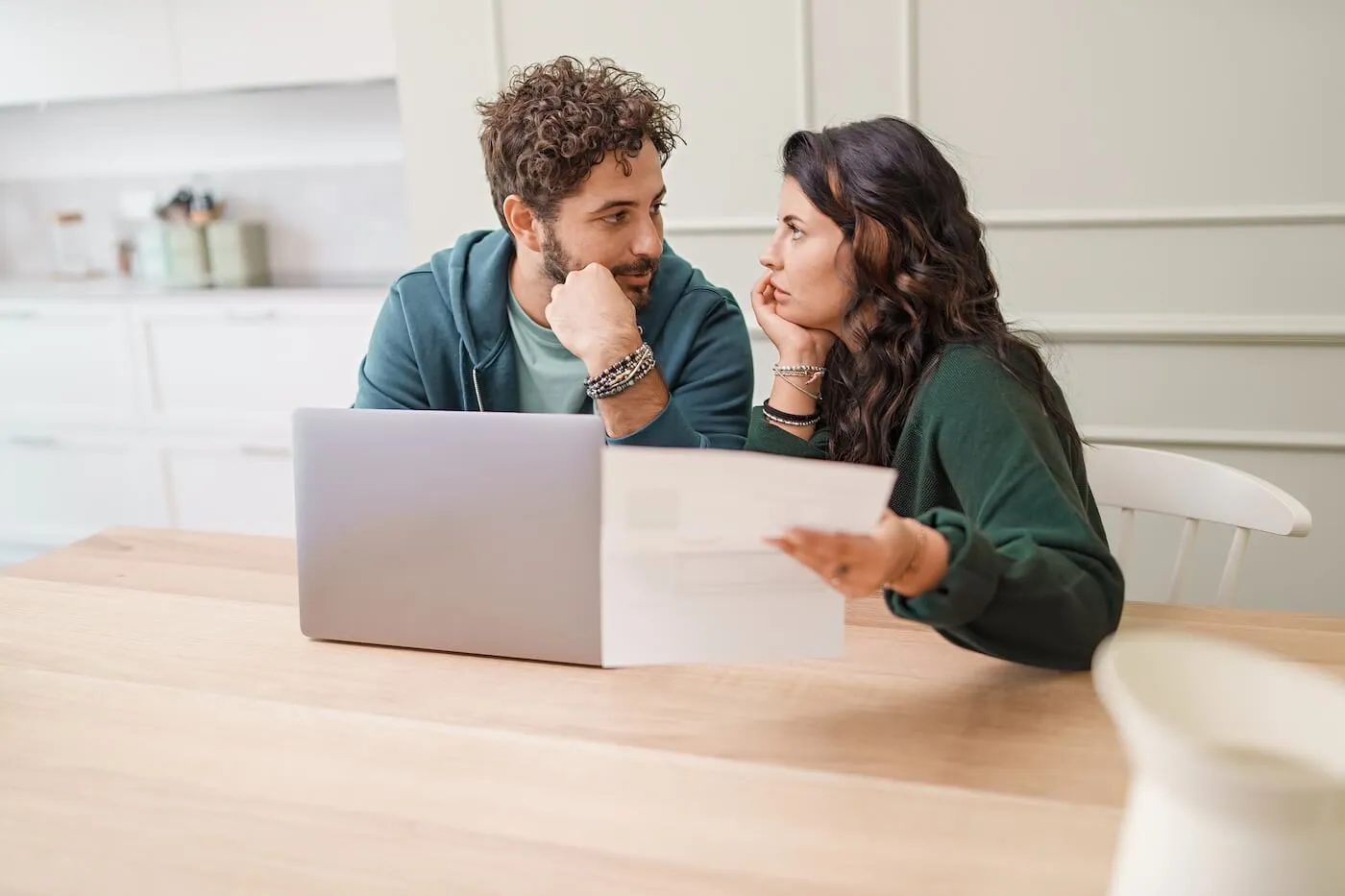 Couple seated at a dining table in a home setting, reviewing a financial document beside an open laptop.