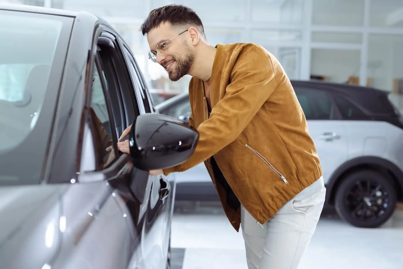 Smiling male customer looking inside a vehicle through the side window at a car dealership