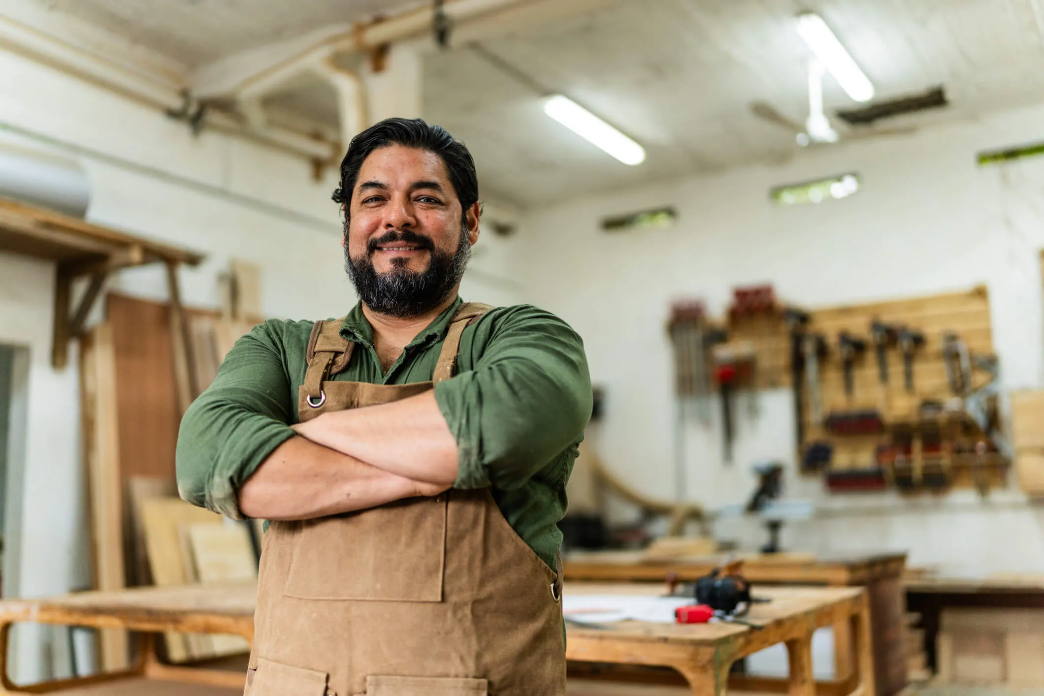 Portrait of a smiling mature carpenter wearing apron and standing in a workshop