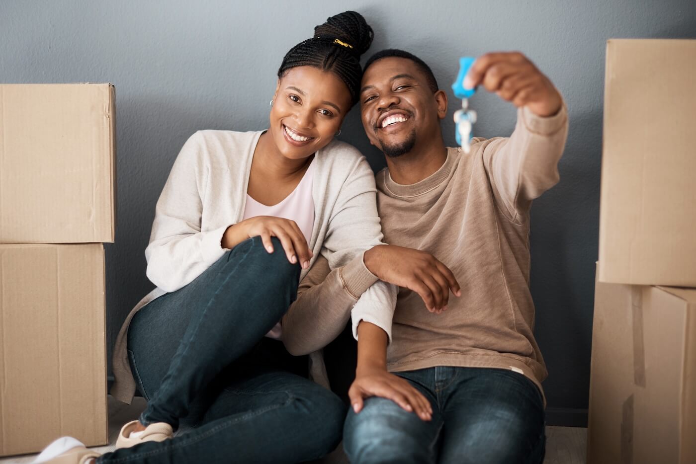 Happy young couple sitting on the floor between the moving boxes and holding the keys from their hew home