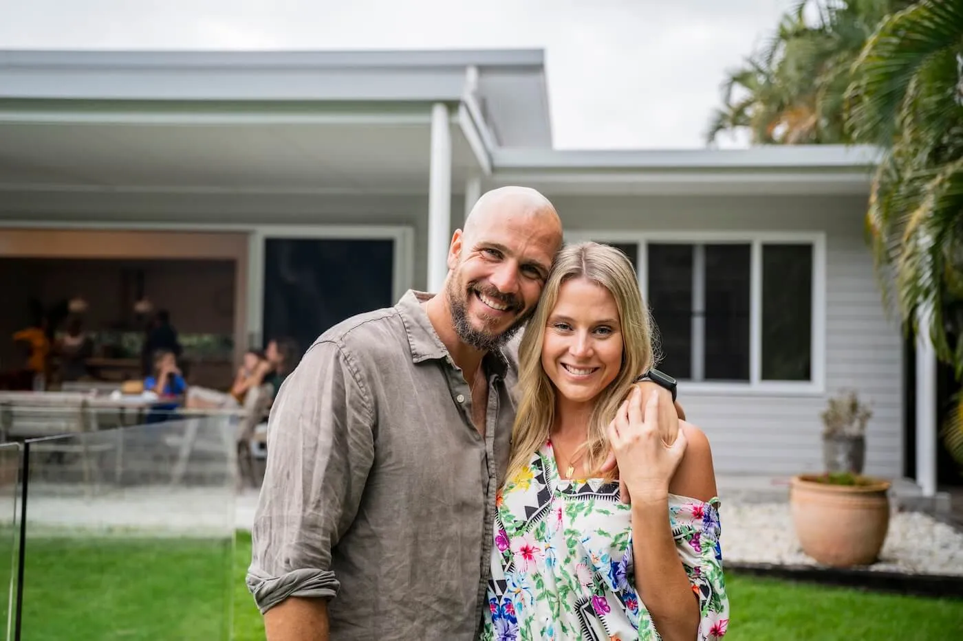 Smiling couple posing for a photo in their backyard while their children play in the background