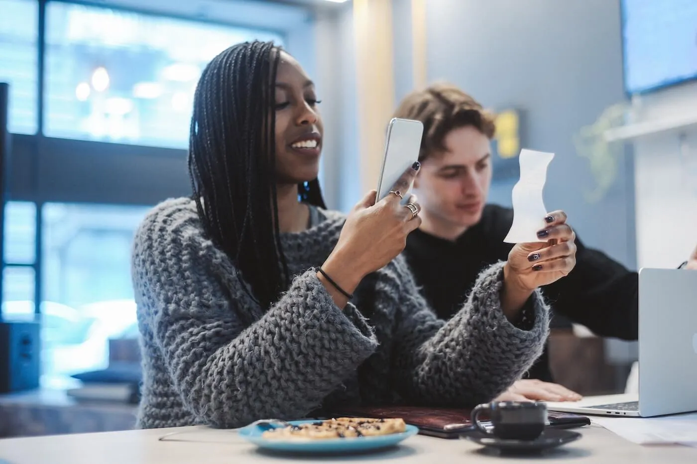 Smiling woman photographing a receipt with her smartphone in a café, seated next to her partner