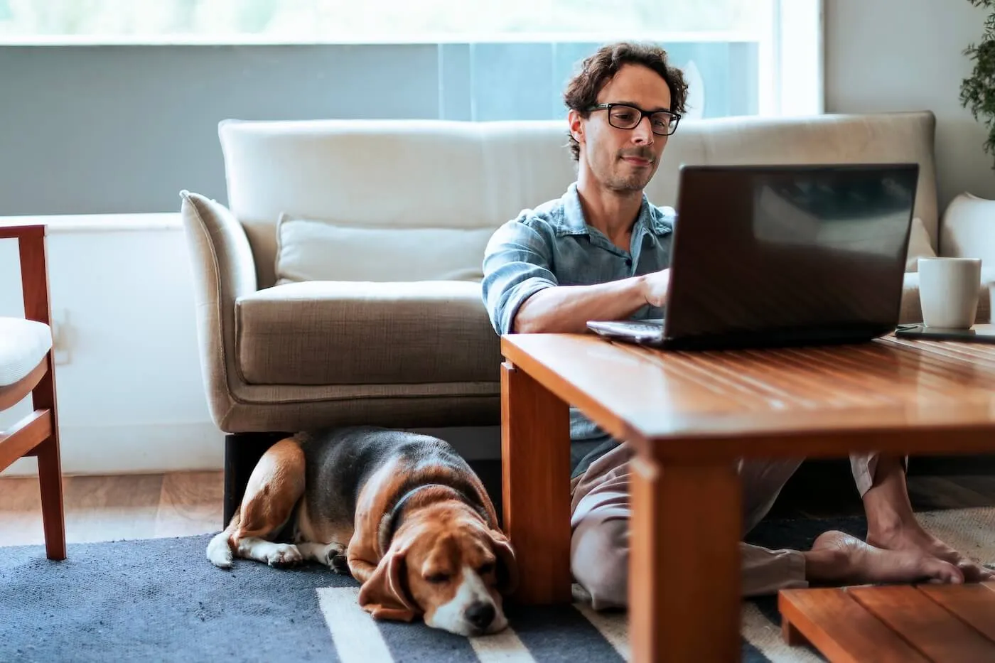 Pensive man using his laptop in the living room, with a dog lying beside him