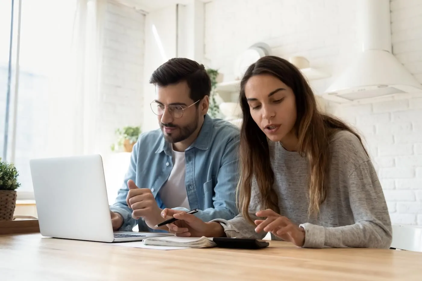 Focused couple planning their finances in the kitchen with an open laptop on the table