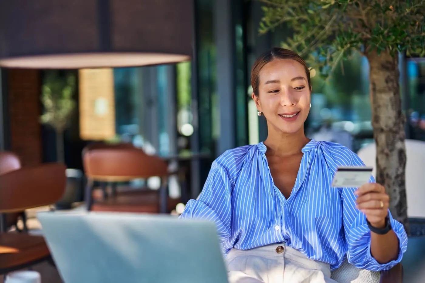 Smiling woman holding a credit card while using her laptop in the outdoor cafe