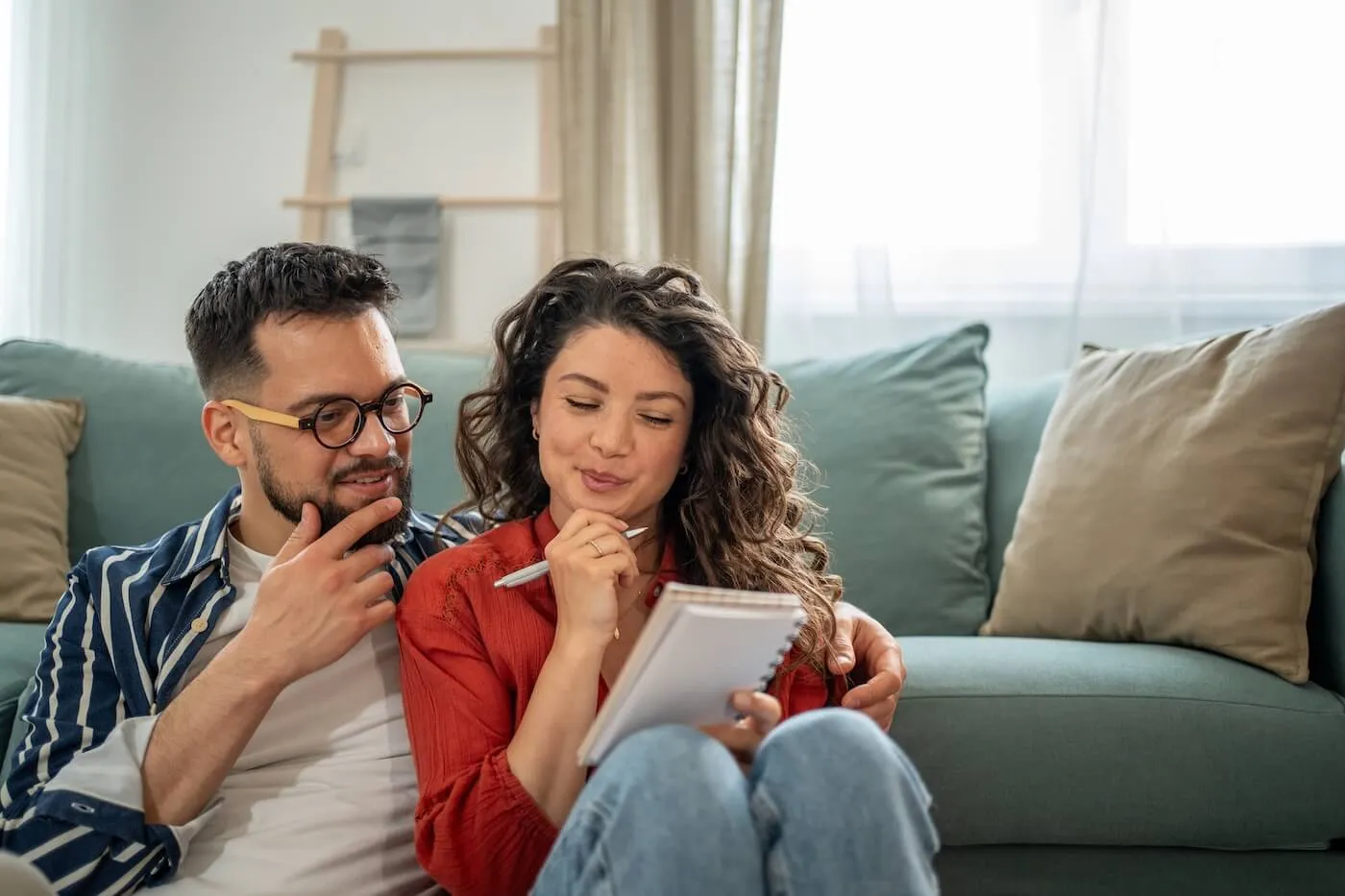 Happy couple sitting together on the floor next to a couch, looking at a notebook as one of them writes