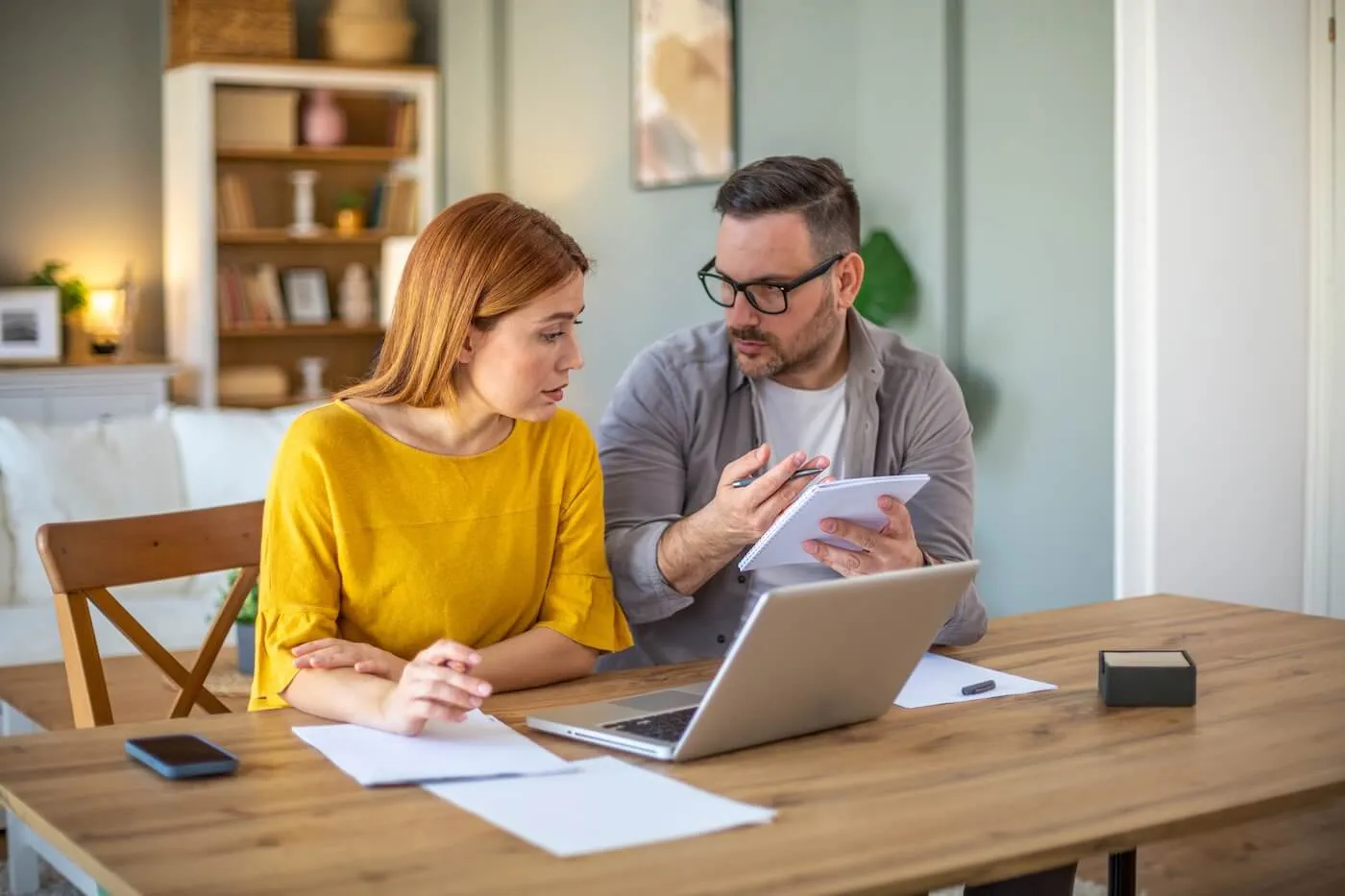 Focused couple planning finances at home, with the printed documents and open laptop on the desk beside them