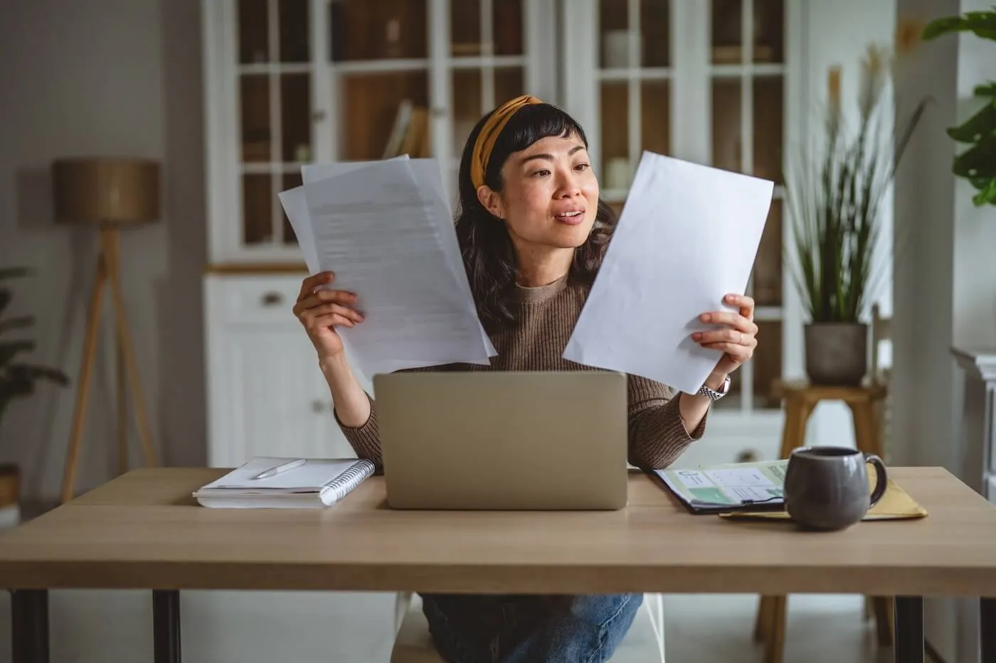 Woman reviewing paperwork while sitting at the desk with an open laptop