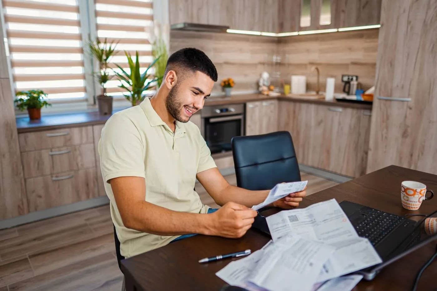 Smiling young man reading his mail in the kitchen