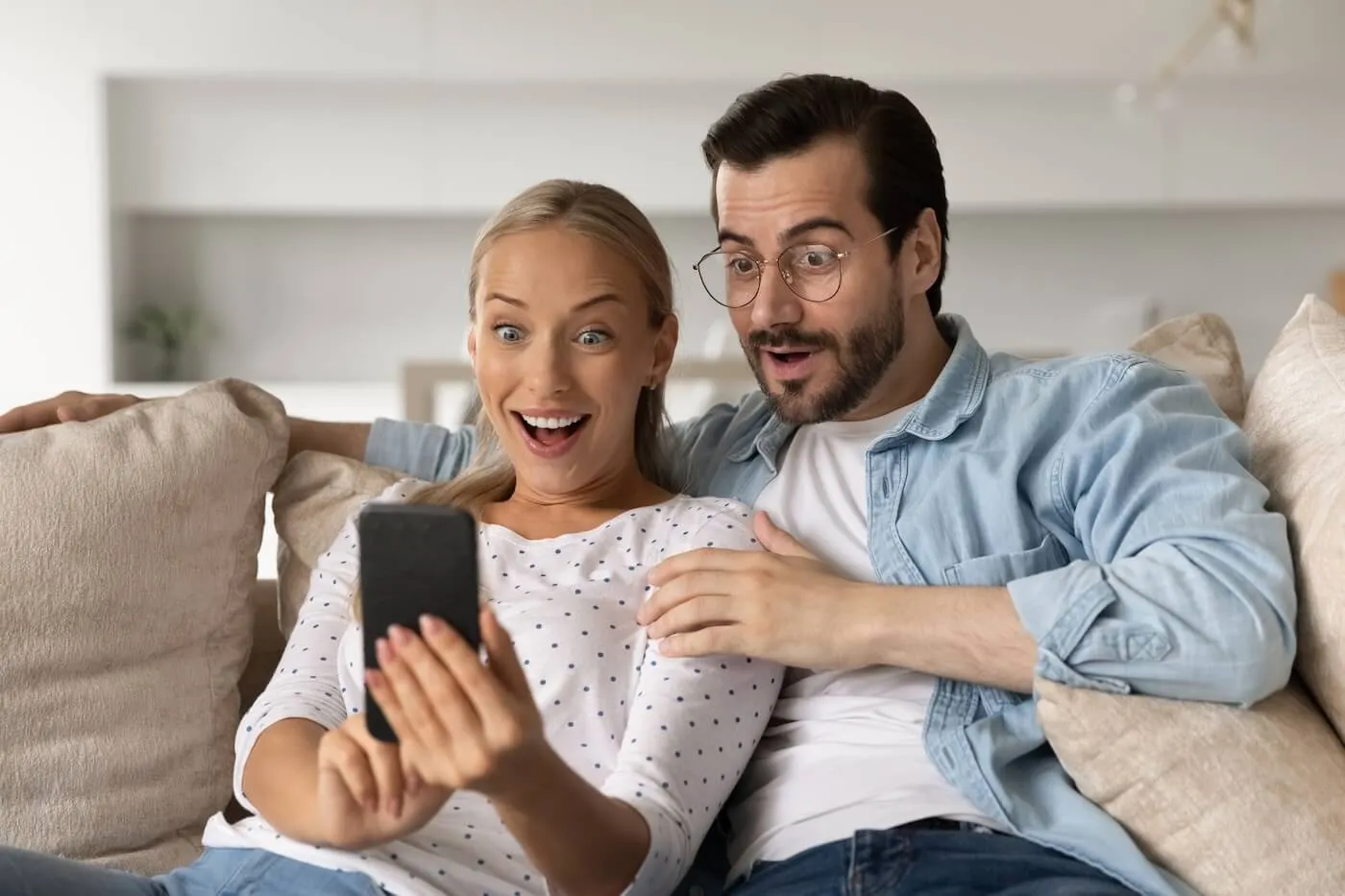 Surprised couple looking at the smartphone while sitting on a sofa