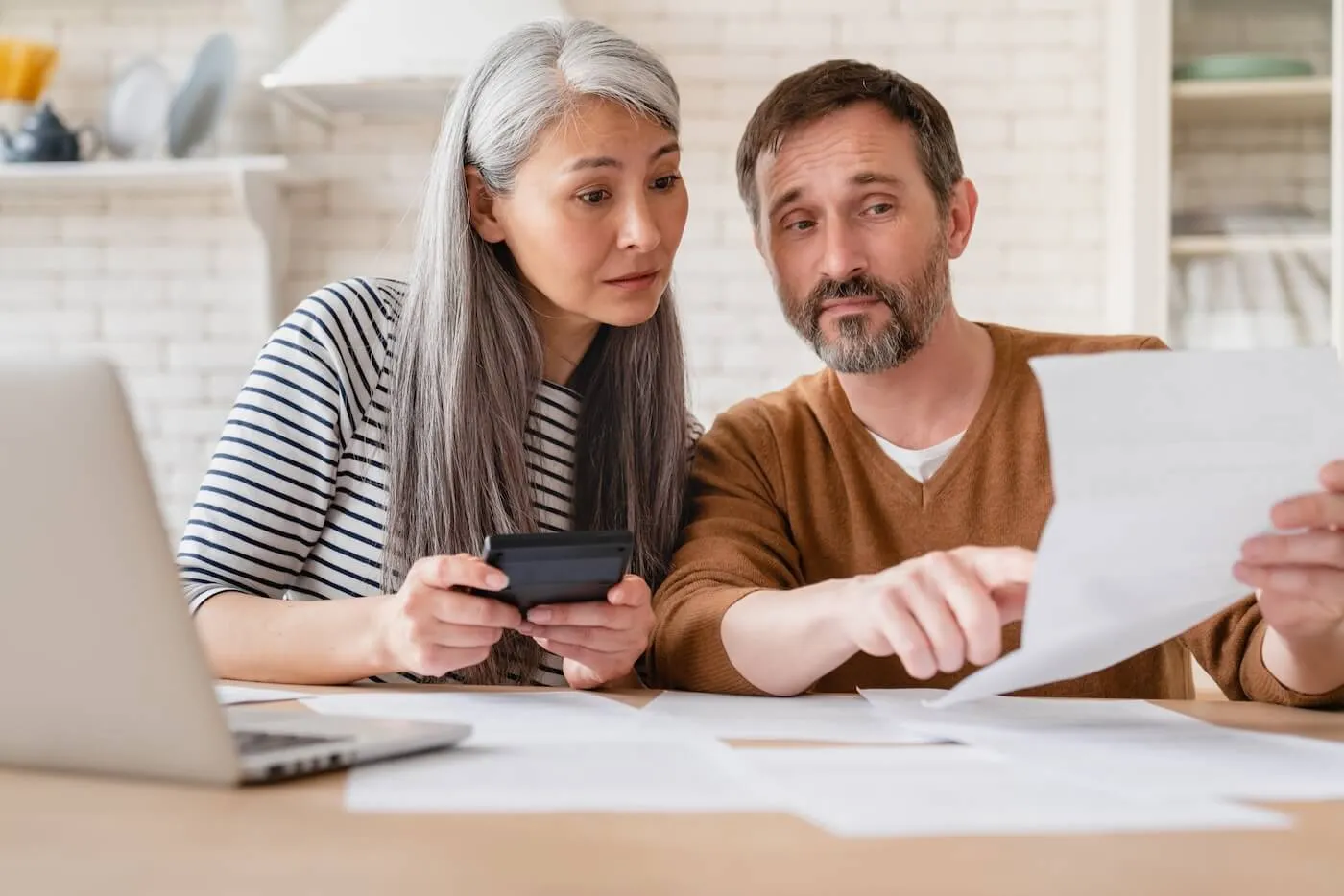 Focused mature couple reviewing printed documents while making calculations