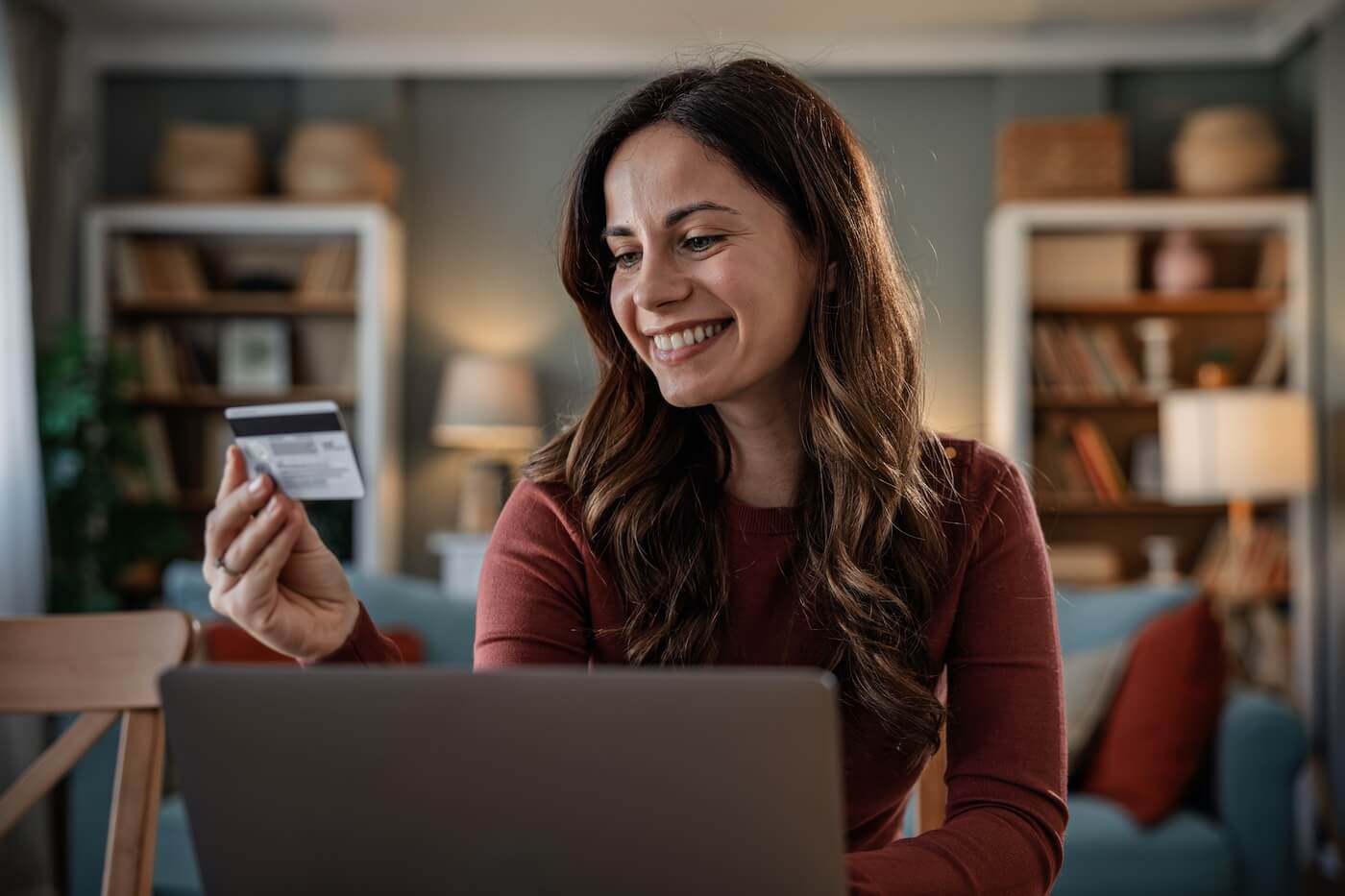 Smiling woman holding a credit card while using her laptop at home