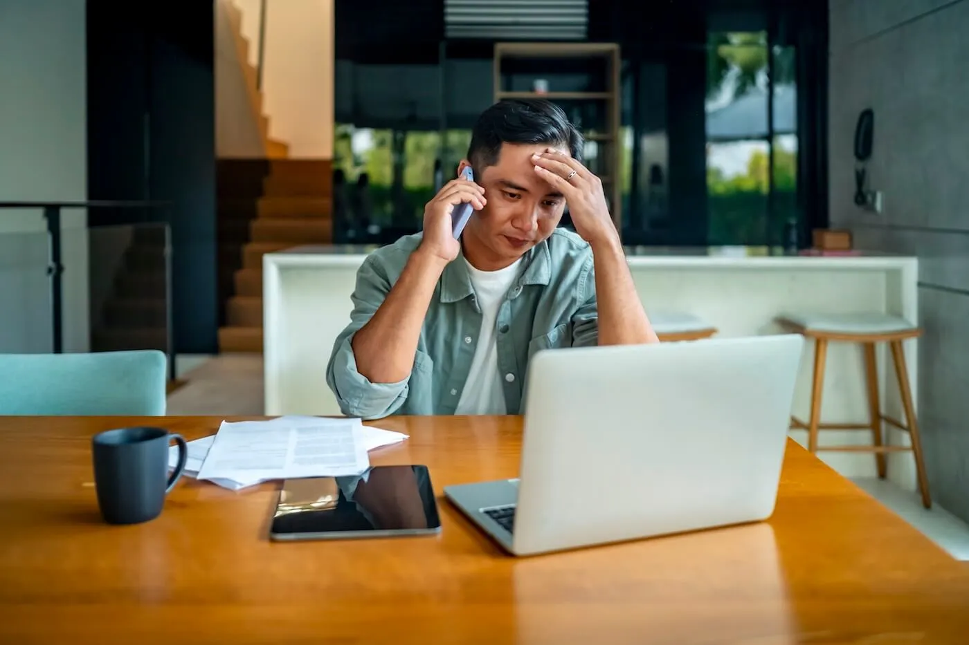 Concerned man making a phone call while using his laptop at home