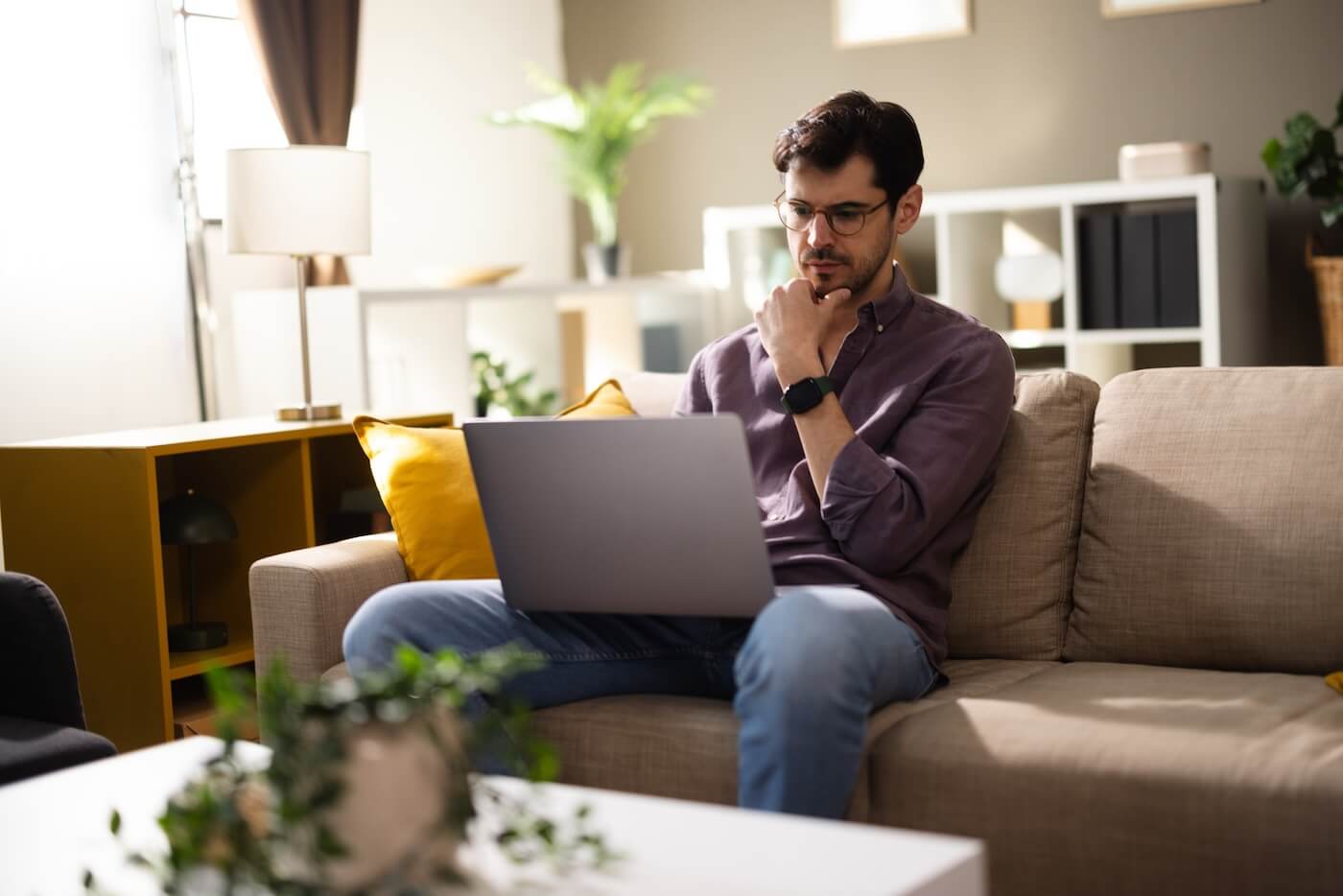 Pensive man sitting on a sofa in the living room with a laptop