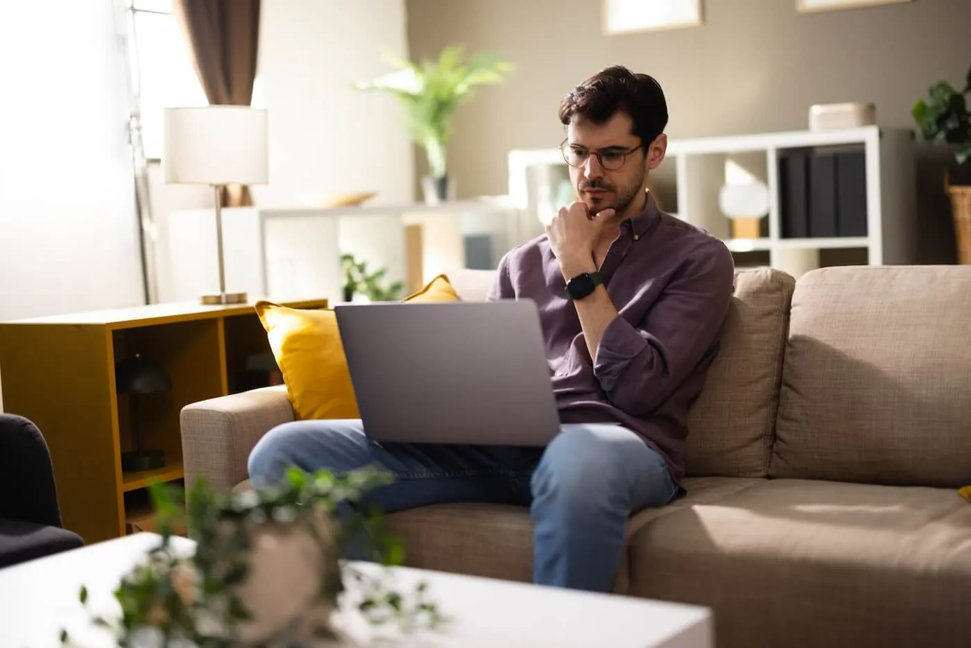 Pensive man sitting on a sofa in the living room with a laptop