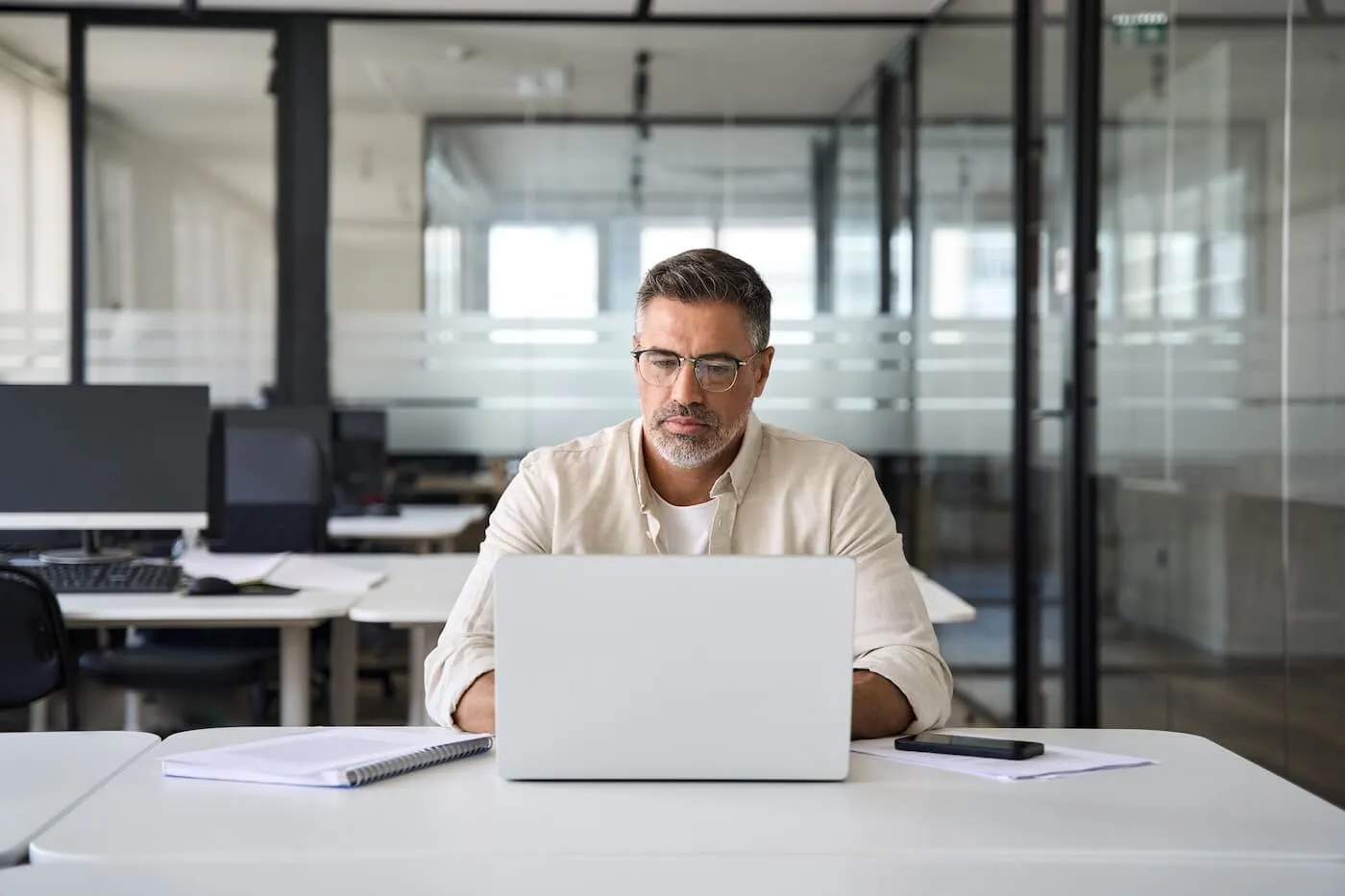 Focused mature man in smart casual attire working on a laptop in a modern office