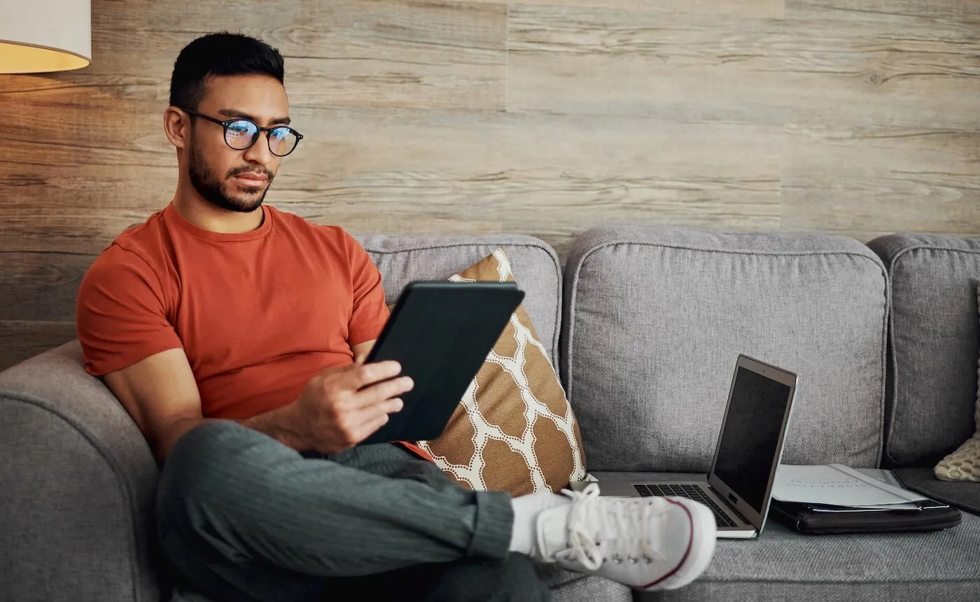 Focused man wearing glasses sitting on a couch and using a tablet