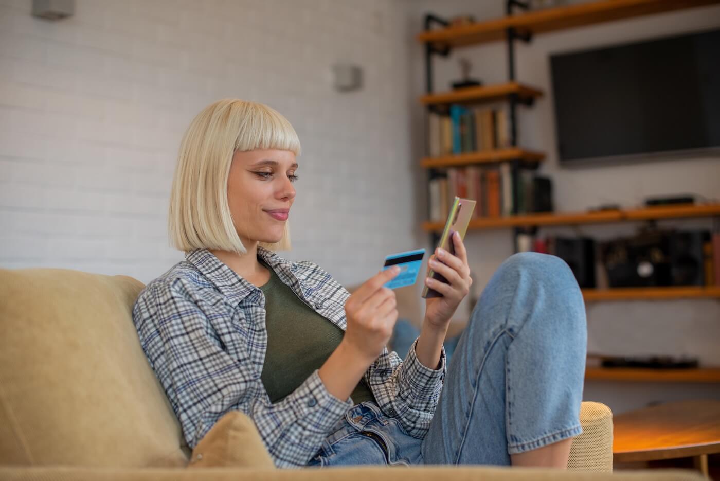 Young woman sitting on a sofa and using her credit card and a mobile phone