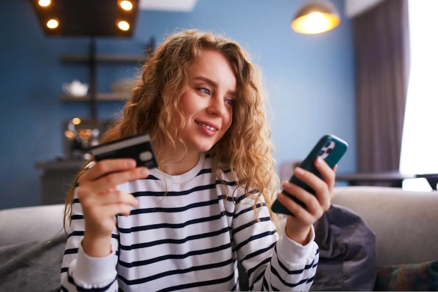Smiling young woman holding a credit card while using her smartphone