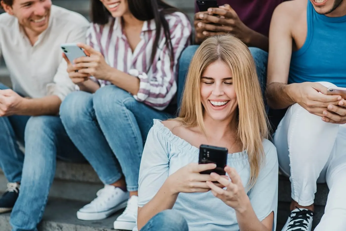 A group of people sitting close together on outdoor steps, all holding smartphones, with a young woman in the foreground looking at her phone.