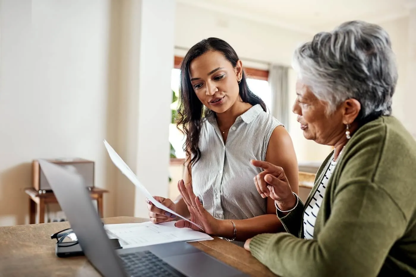 Two women sitting at a table reviewing documents together, with a laptop open in front of them