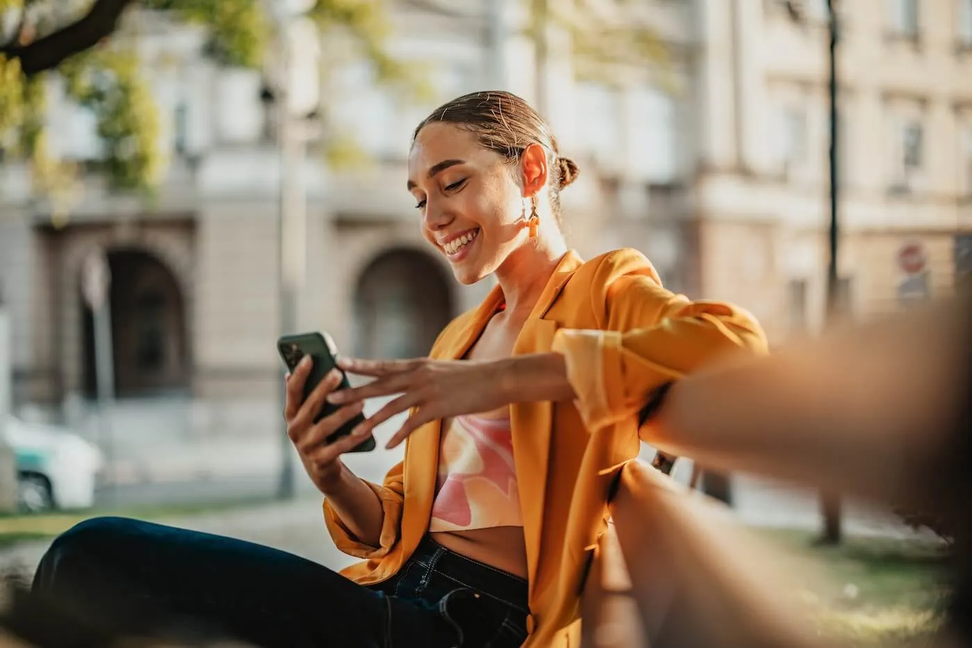Smiling young woman using her smartphone while sitting on an outdoor bench