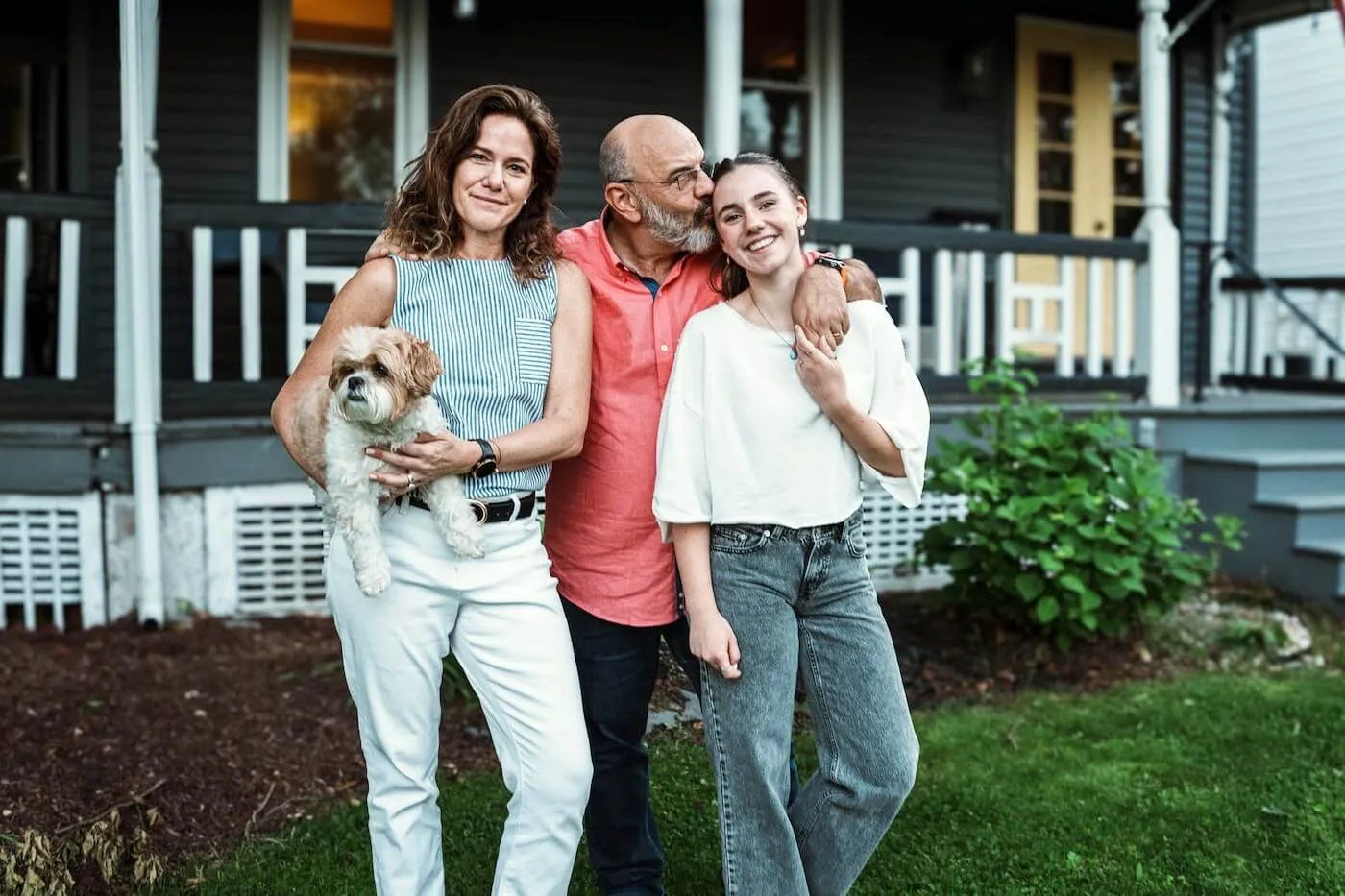 Happy family of three with a small dog posing for a photo in front of their house