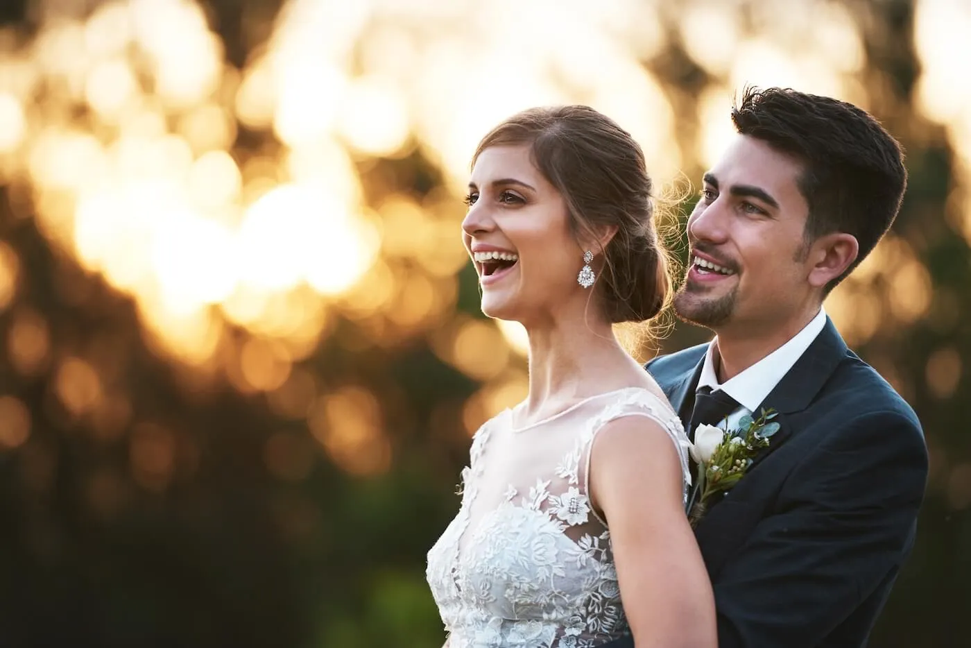 Happy bride and groom standing together outdoors at sunset