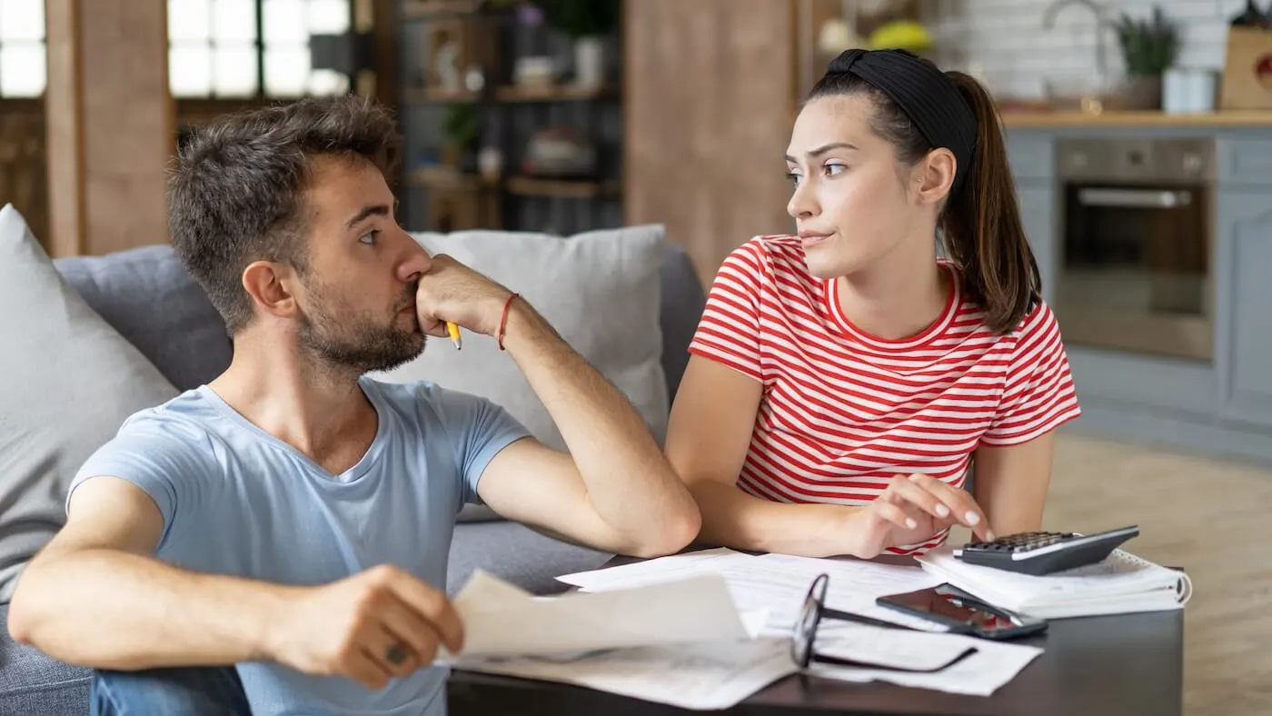 Concerned couple looking at each other while reviewing their finances