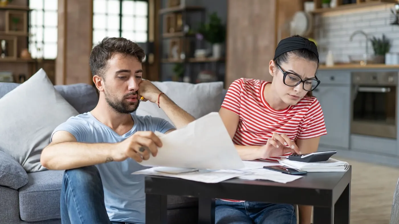 Concerned young couple looking at the printed documents and making calculations in the living room