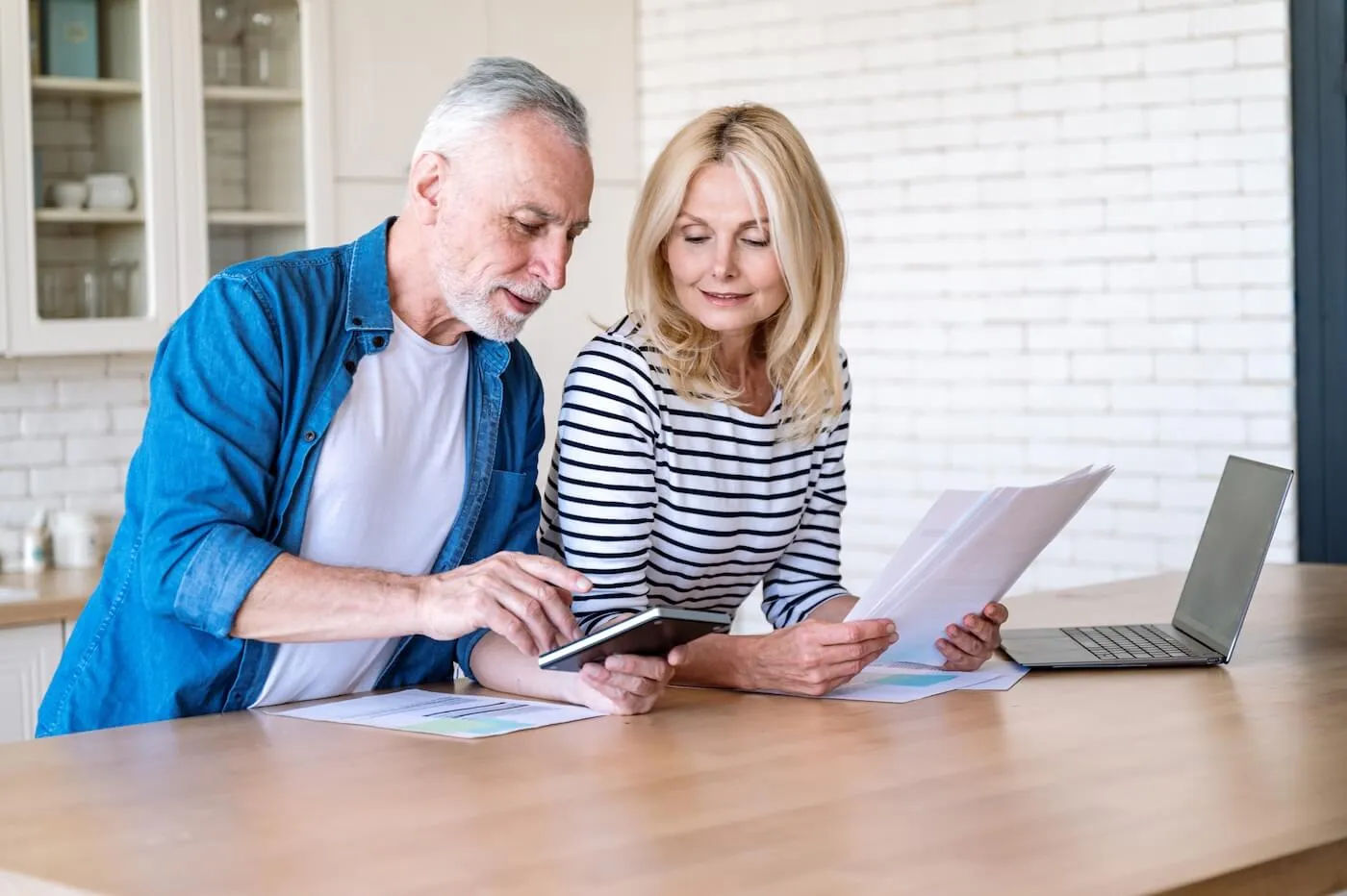 Senior couple planning their budget, with the woman holding the printed documents and the man making calculations