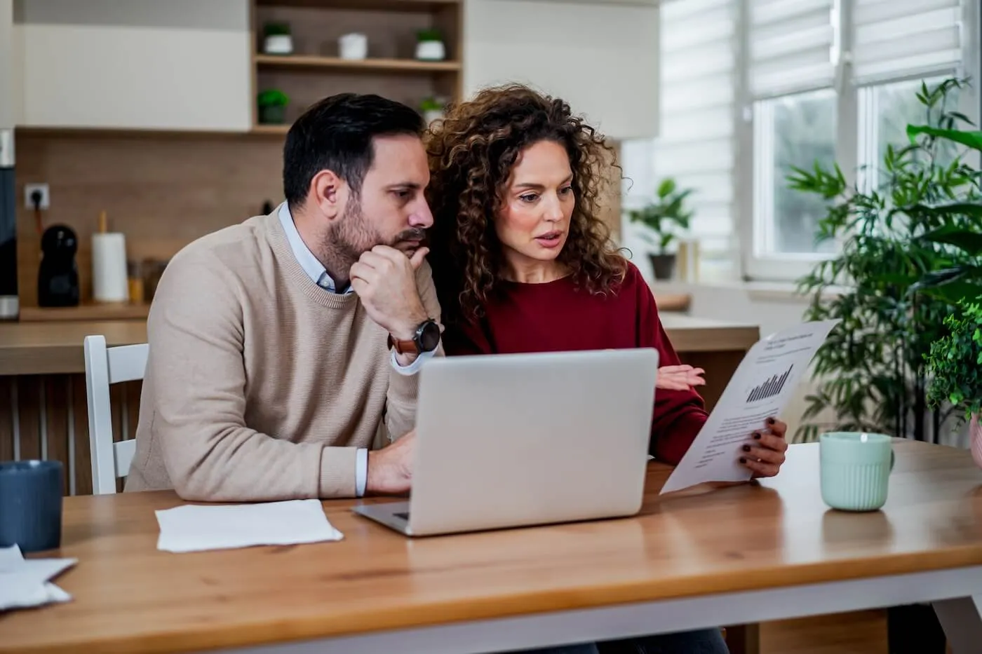 Concerned couple reviewing the printed bills, with an open laptop on the desk