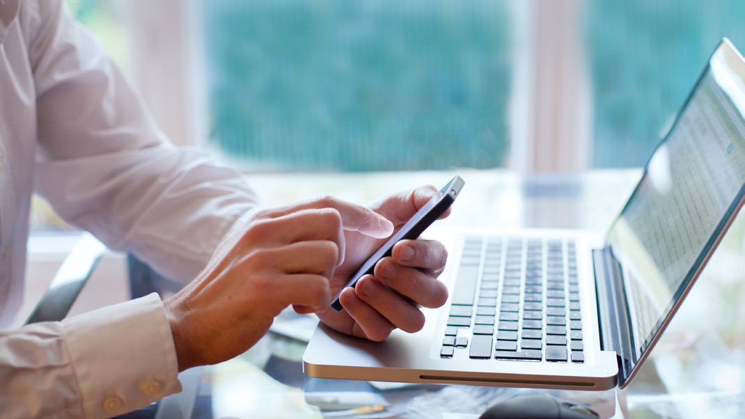 man typing on mobile device at his laptop - automating credit decisions.