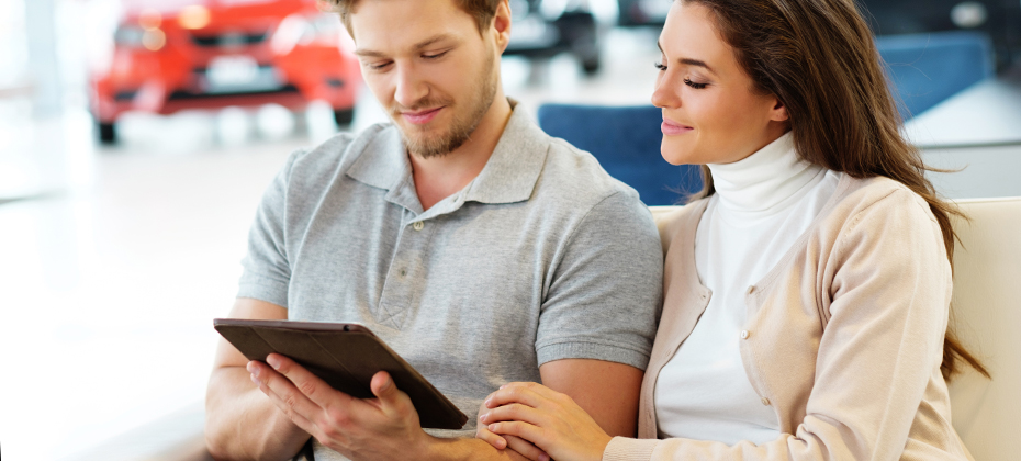 Young couple looking at tablet in car dealership