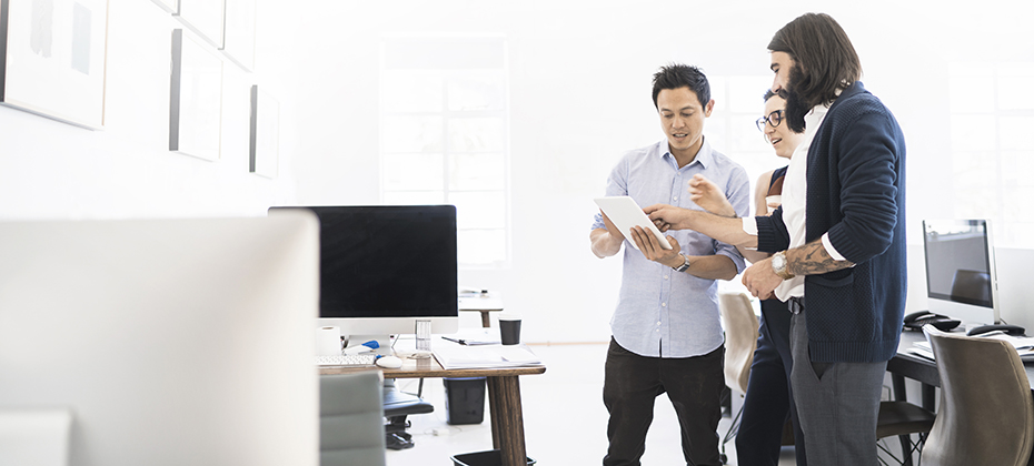 Professionals are working in office, gathered around a tablet.