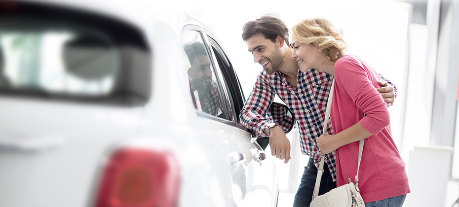 Happy couple looking a new car in car dealership saloon