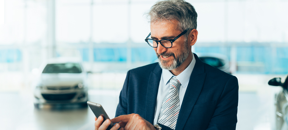 Automotive dealer in showroom looking at mobile phone