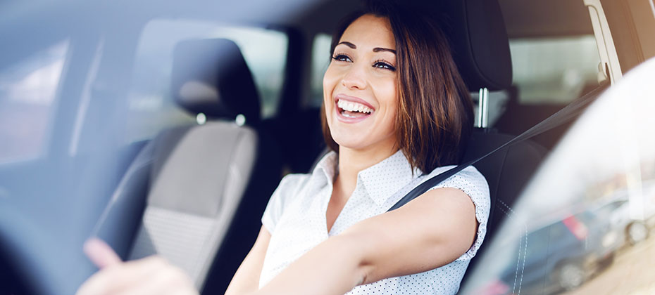 Smiling brunette driving her car. Hands are on steering wheel.