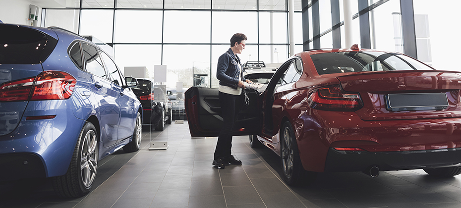 Senior woman looking inside car in showroom