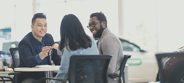 Young couple discuss the purchase of a new car with salesman