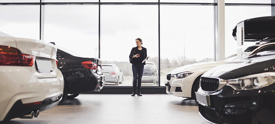 Full length of woman standing amidst cars in showroom