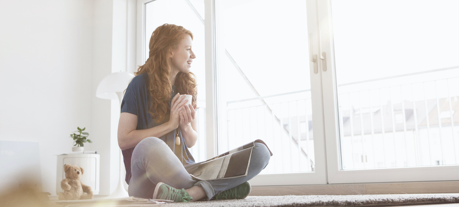 Young woman sitting on the floor of her living room looking through window