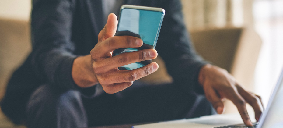 Man using a smartphone and a laptop while working from home