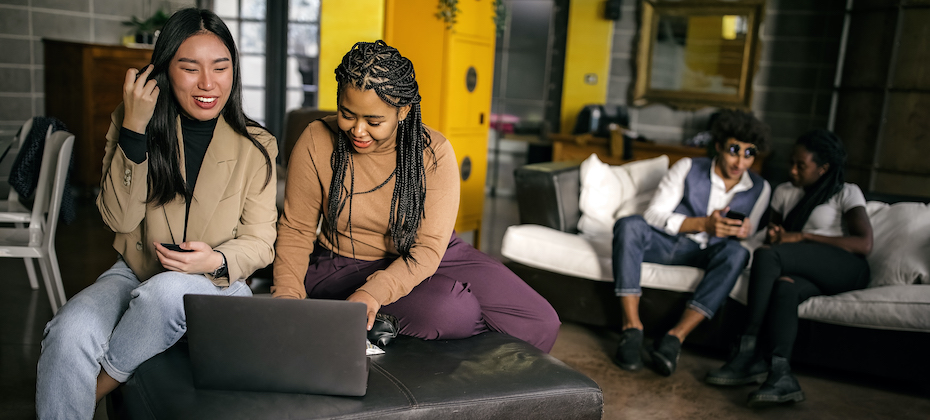 Asian and Black women looking down and smiling at laptop