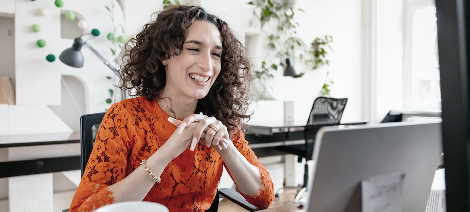 A transgender woman smiling while video calling a business partner using her laptop at the office.